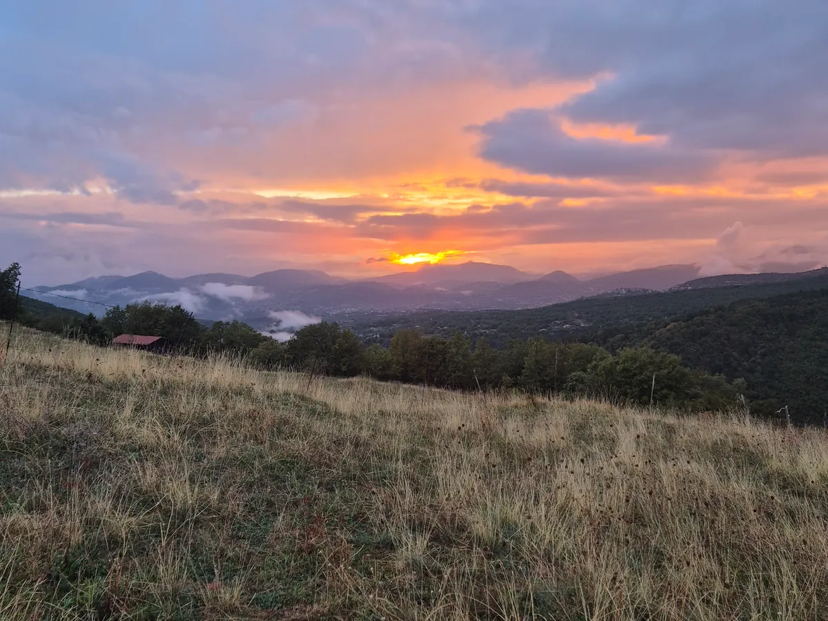 Abendhimmel über einer Wiese und bewaldeten Hügeln.